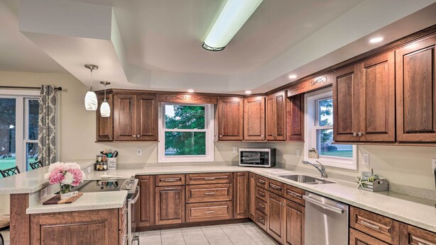 A modern kitchen with wooden cabinets, a central island, stainless steel appliances, and a large window providing natural light. - Cozy Seneca Falls Home Close to Cayuga Wine Trail! (Seneca Falls)