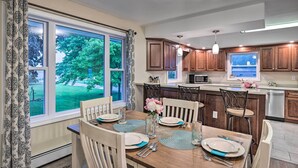 A modern kitchen with wooden cabinets, a large island, and a dining area with a table set for four. - Cozy Seneca Falls Home Close to Cayuga Wine Trail! (Seneca Falls)