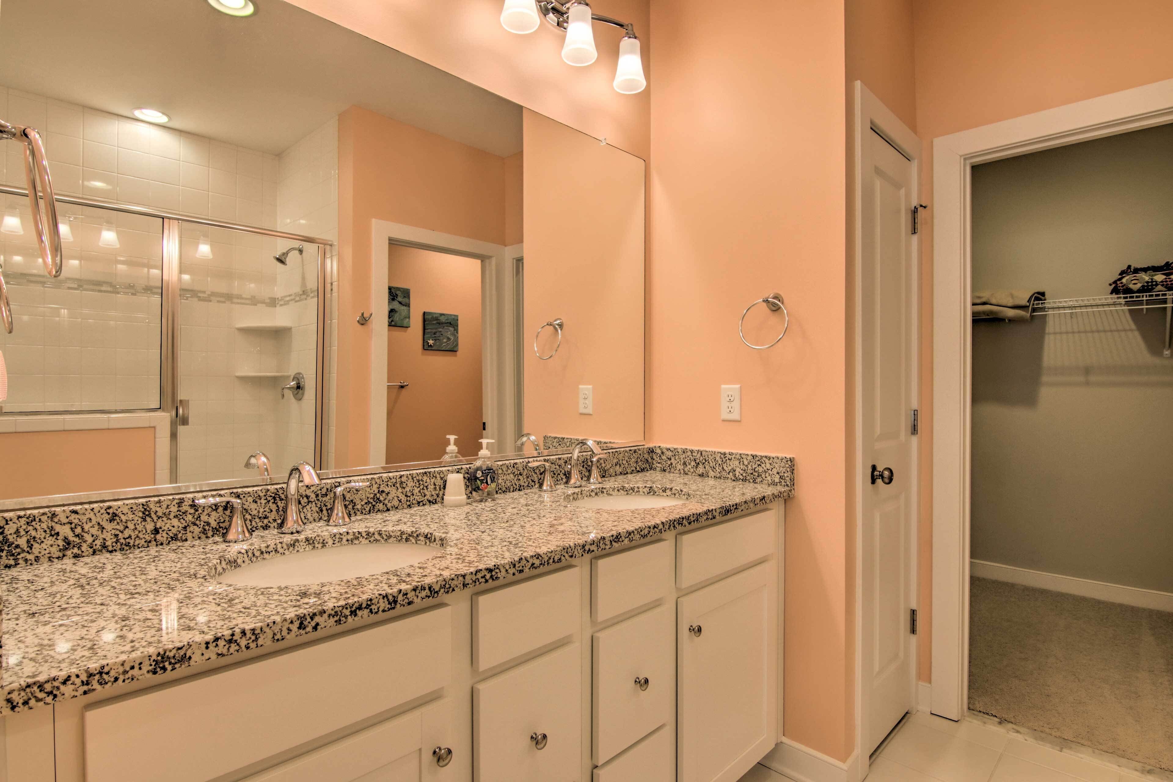 Une salle de bain avec un lavabo sur un plan de travail en granit, un grand miroir et une douche à l’italienne.
