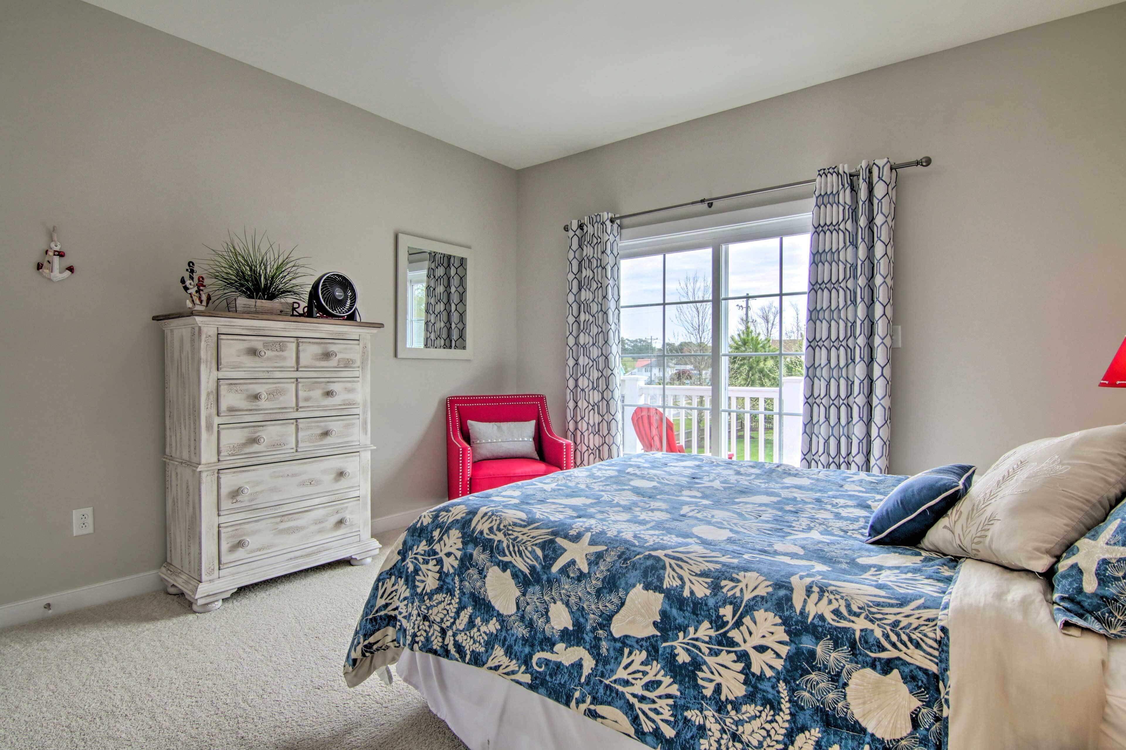 A bedroom with a bed, a dresser, a red chair, and a window with patterned curtains.