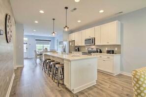 A modern kitchen with white cabinetry, a central island with stools, and pendant lighting.