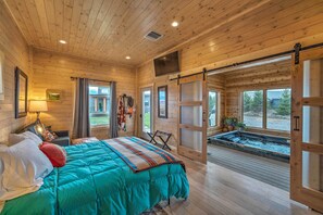 Une chambre dans un chalet en bois, avec un lit, une télévision et une fenêtre donnant sur un jacuzzi.