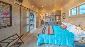 A wooden interior with a bed, a bathroom, and a kitchen area. - Ennis Lake Studio w/ Kayak, Pool & Fire Pit! (McAllister)