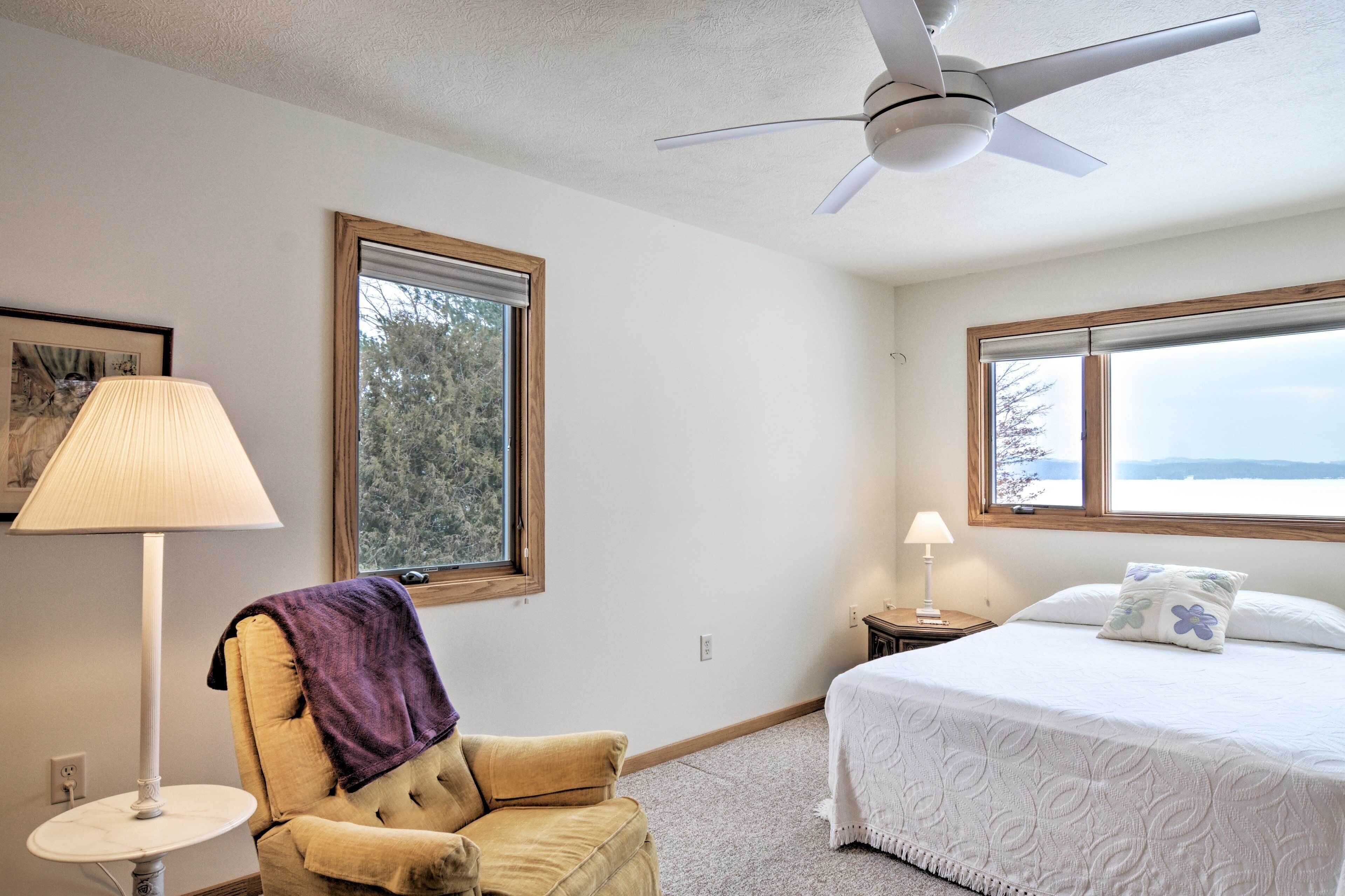 A bedroom with a bed, a chair, a ceiling fan, and two windows.