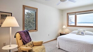 A bedroom with a bed, a chair, a ceiling fan, and two windows. - Cedar Cottage, Private Beach on Lake Leelanau (Cedar)
