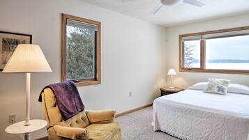 A bedroom with a bed, a chair, a ceiling fan, and two windows.