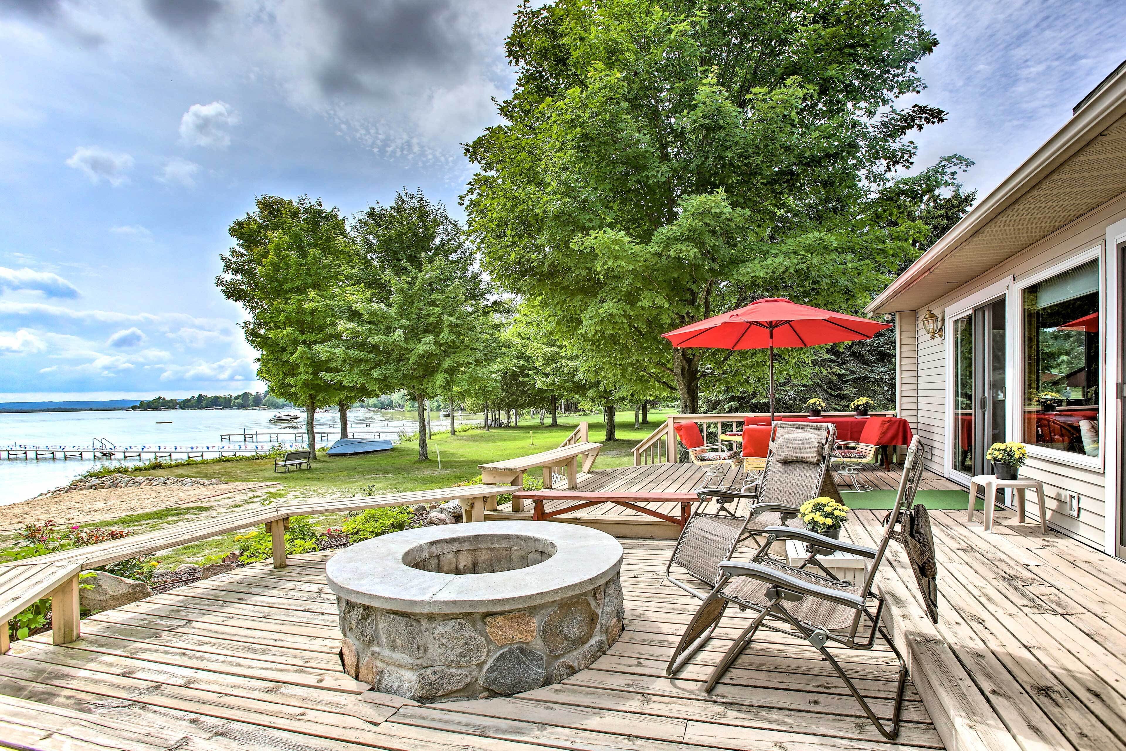 A wooden deck with a stone fire pit, outdoor furniture, and a red umbrella.