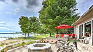 A wooden deck with a stone fire pit, outdoor furniture, and a red umbrella. - Cedar Cottage, Private Beach on Lake Leelanau (Cedar)