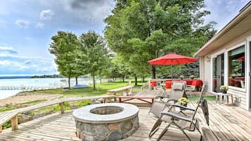 A wooden deck with a stone fire pit, outdoor furniture, and a red umbrella.