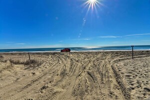 Una playa con marcas de neumáticos que conducen a un vehículo rojo estacionado cerca del agua.