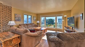 A living room with a brick wall, two sofas, a wooden coffee table, and large windows with a view of the outside.