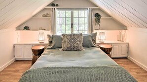 Um quarto de sótão acolhedor com uma cama grande, duas mesas de cabeceira com abajures, uma janela com cortinas e um teto inclinado.