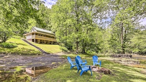 Uma cabana com varanda e uma pequena escadaria que a acessa, rodeada por vegetação exuberante e um lago.