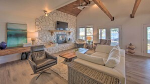 A spacious living room with a stone fireplace, leather sofa, and a large flat-screen TV mounted on the wall. - Stunning Lakefront Home: Hot Tub & Game Room! (Mabank)