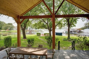 A wooden deck with a table and chairs, overlooking a grassy area with trees and a body of water.