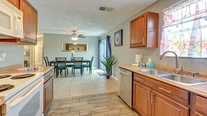 A kitchen with wooden cabinets, a microwave, a stove, a sink, and a dining area with chairs and a table.