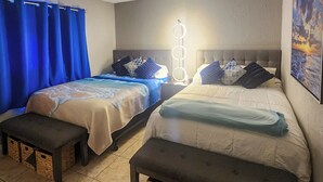 A room with two beds, each with a headboard, a bench, and a wall-mounted light fixture.