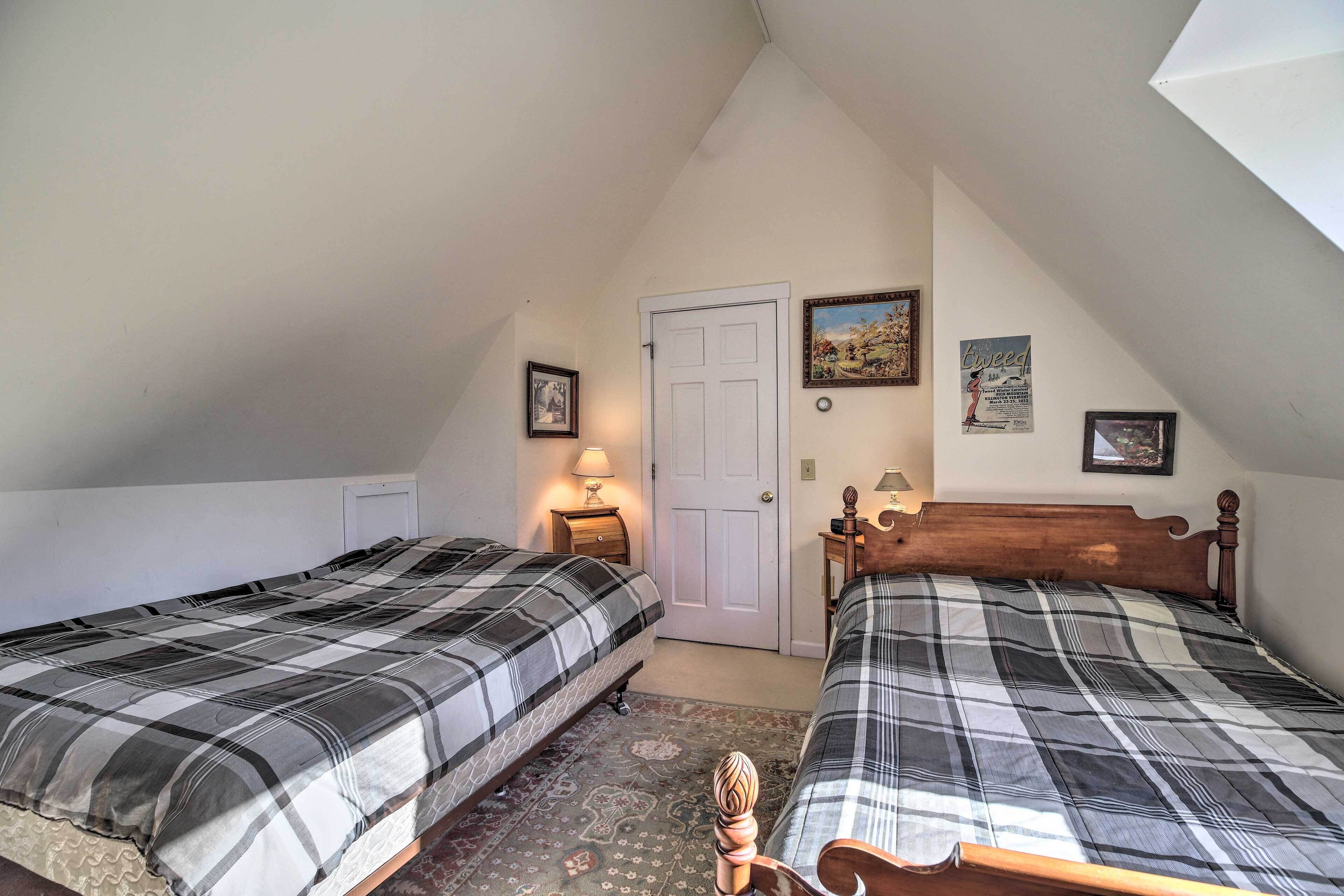 A bedroom with two beds, a door, and a small table with a lamp.