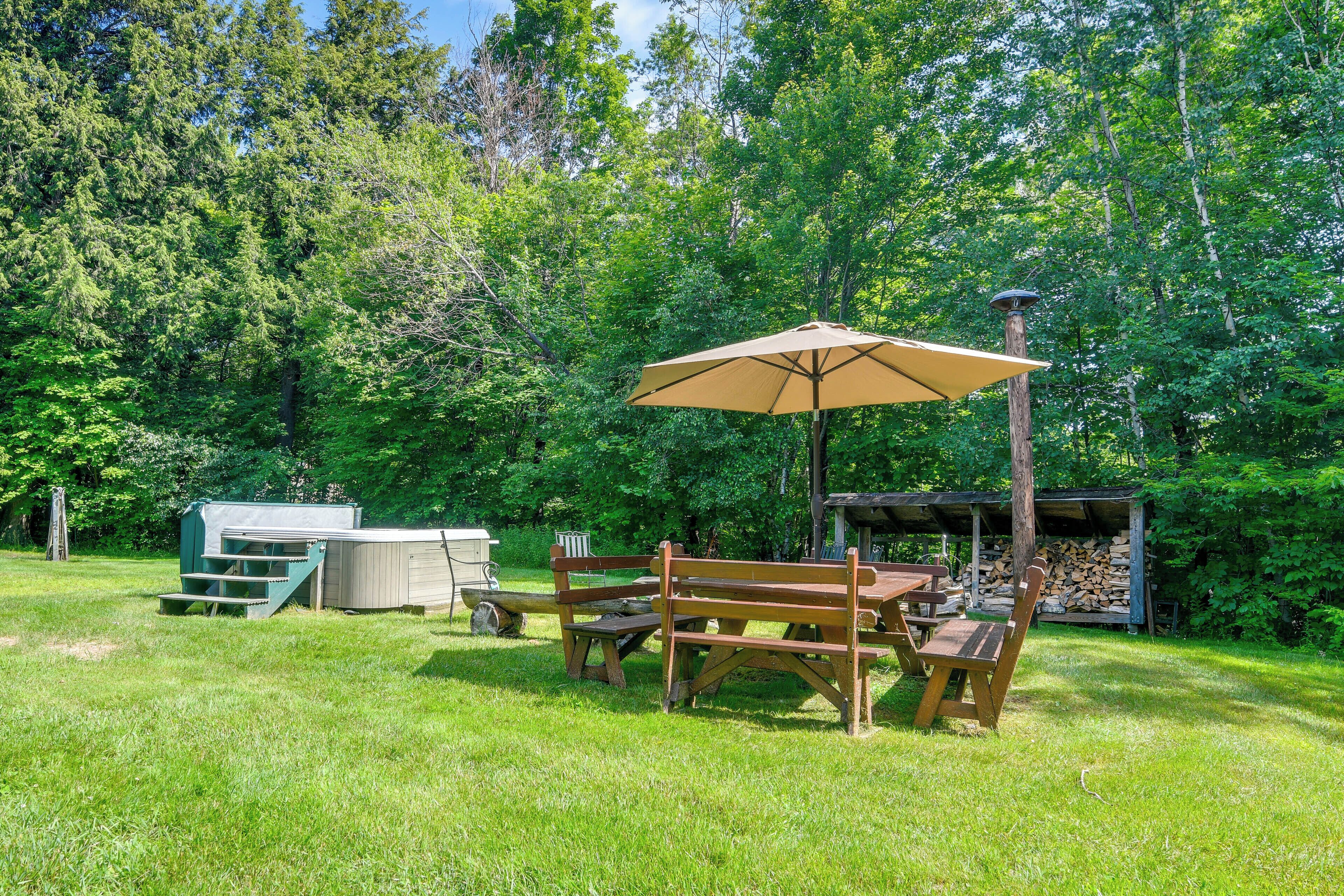 A picnic setup with a table, benches, and an umbrella in a grassy area with trees in the background.