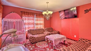 A room with a red wall, a television mounted on the wall, a chandelier, a sofa, a table, and a mosquito net. - Pet-friendly Des Moines Home w/ Fenced Yard! (Des Moines)