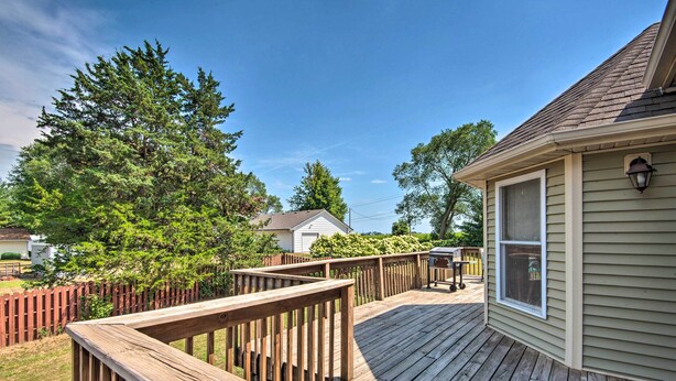 A wooden deck with a railing, a house with a window, and a large tree in the background. - Pet-friendly Des Moines Home w/ Fenced Yard! (Des Moines)