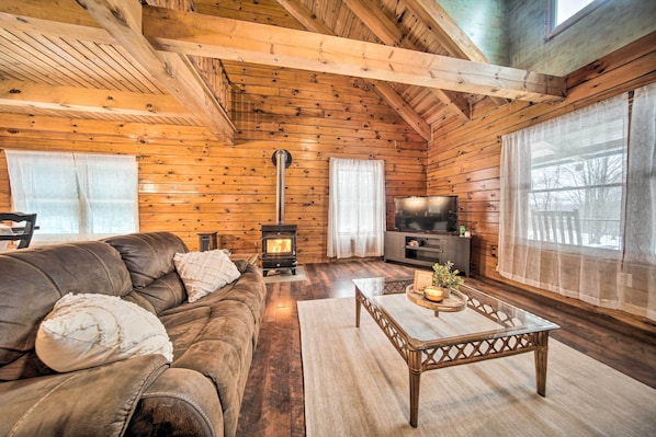 Un acogedor interior de cabaña de madera con un sofá de cuero, una mesa de centro de vidrio, una chimenea y un televisor.