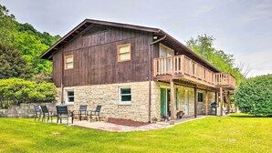 A two-story house with a stone foundation and wooden upper structure, featuring a balcony and outdoor seating area. - Richwood Respite Near Trout Fishing (Richwood)