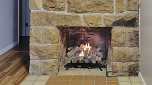 A stone fireplace with logs burning, a tiled floor, and a wooden floor in the background. - Richwood Respite Near Trout Fishing (Richwood)