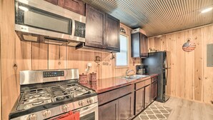 A kitchen with wooden cabinets, stainless steel appliances, and a patterned rug. - Charming New Concord Cabin on 50-acre Farm! (New Concord)