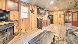 A rustic interior with wooden walls, a fireplace, a kitchen area, and a seating area with a couch and a coffee table. - Charming New Concord Cabin on 50-acre Farm! (New Concord)