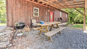 A rustic wooden building with a covered patio area, a barbecue grill, and picnic benches. - Charming New Concord Cabin on 50-acre Farm! (New Concord)