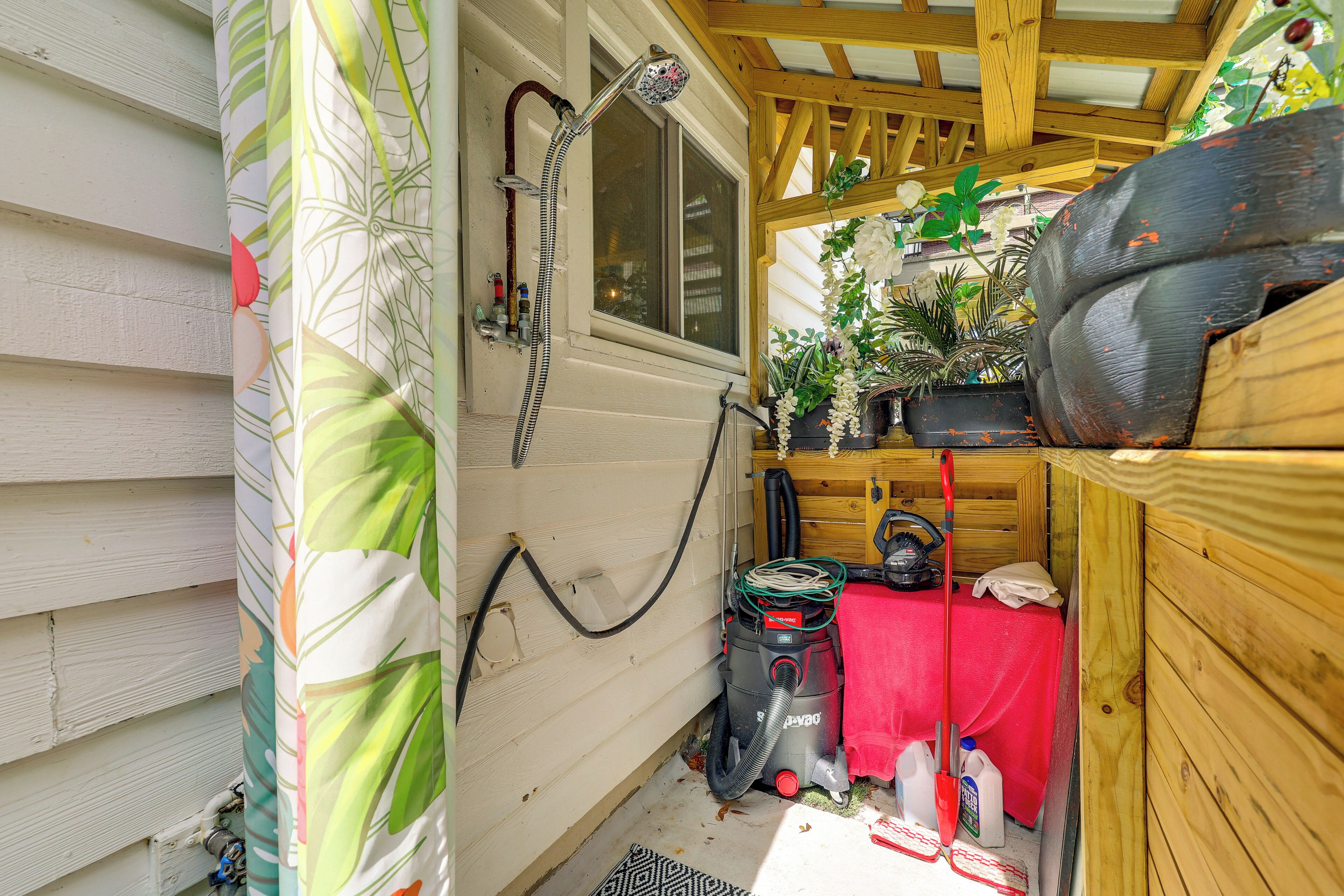 A small, enclosed outdoor shower area with a hose, a vacuum cleaner, and a red table.