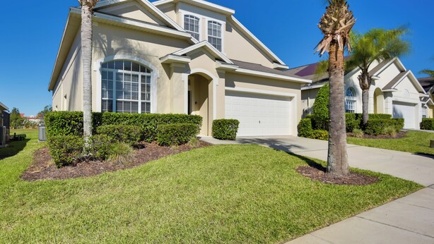 A two-story house with a garage, a covered front porch, and a well-maintained lawn with palm trees. - Family Retreat w/ Pool: 10 Mi to Disney! (Clermont)