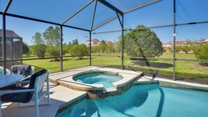 A covered outdoor swimming pool with a hot tub, surrounded by a metal fence, and a view of a residential area with houses and trees. - Family Retreat w/ Pool: 10 Mi to Disney! (Clermont)