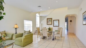 A spacious living area with a green sofa, a glass coffee table, and a dining table with chairs. There is a staircase leading to another level, and the room has a tiled floor. - Family Retreat w/ Pool: 10 Mi to Disney! (Clermont)