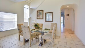 A dining area with a glass table and four chairs, a vase with flowers, and two framed pictures on the wall. - Family Retreat w/ Pool: 10 Mi to Disney! (Clermont)