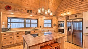 A wooden cabin-style kitchen with a central island, stainless steel appliances, and large windows.