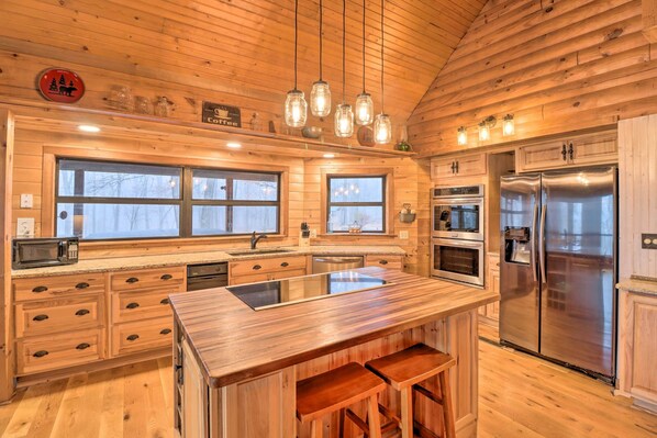 Una cocina estilo cabaña de madera con una isla central, electrodomésticos de acero inoxidable y ventanas amplias.