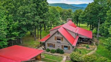 A log cabin with a red roof, surrounded by lush greenery and trees, with a view of distant mountains.