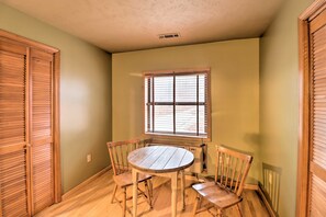 Un comedor con una mesa redonda de madera y cuatro sillas, una ventana con persianas, y paredes y puertas de madera.