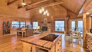 A spacious wooden cabin interior with a large kitchen island, dining area, and a fireplace.