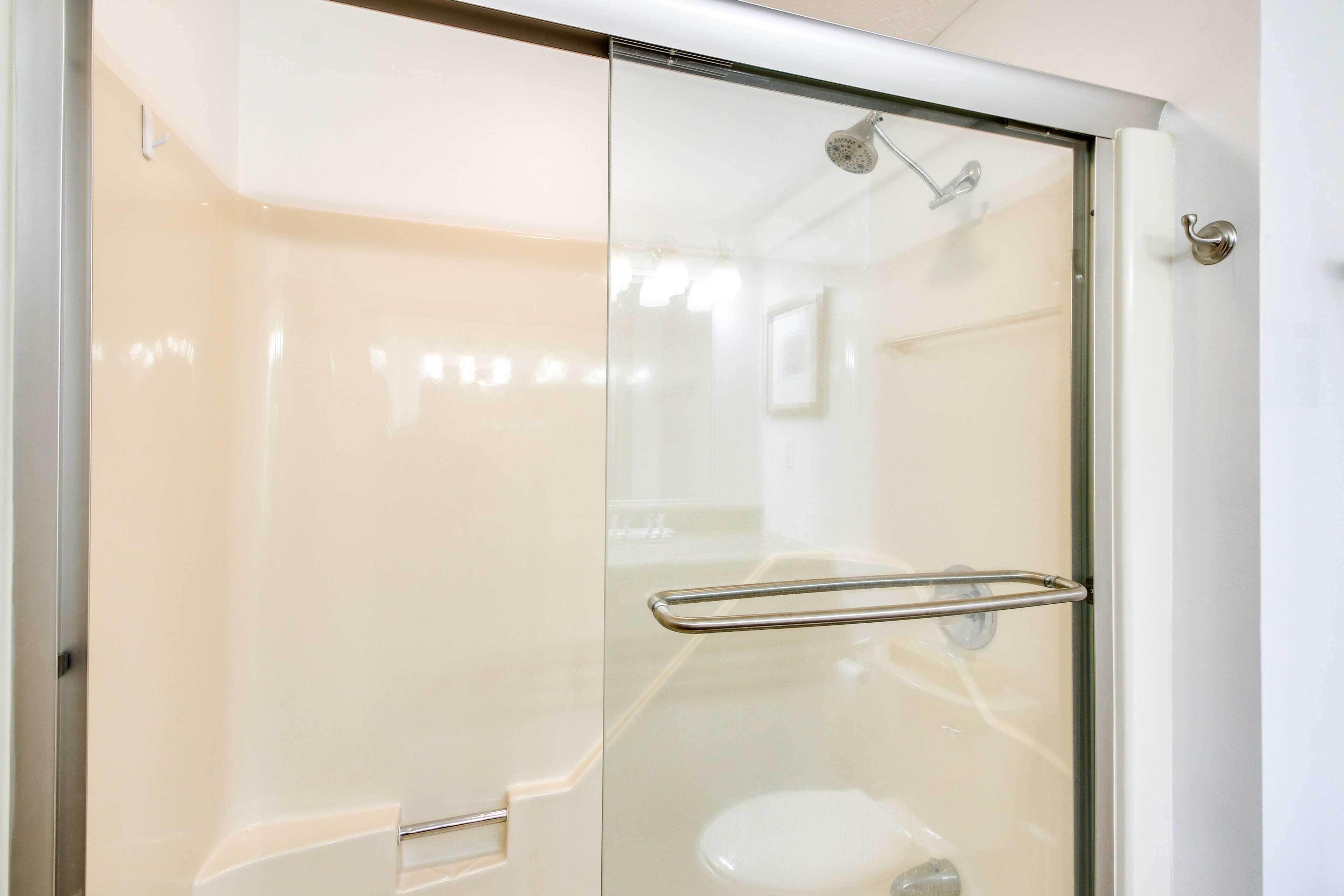 A modern bathroom with a glass shower enclosure, a stainless steel showerhead, and a glass door handle.
