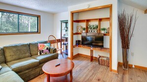 A living room with a sofa, a coffee table, a TV on a wooden stand, and a large window. - 1 Mi to Downtown Conway: Spacious Family Condo! (North Conway)