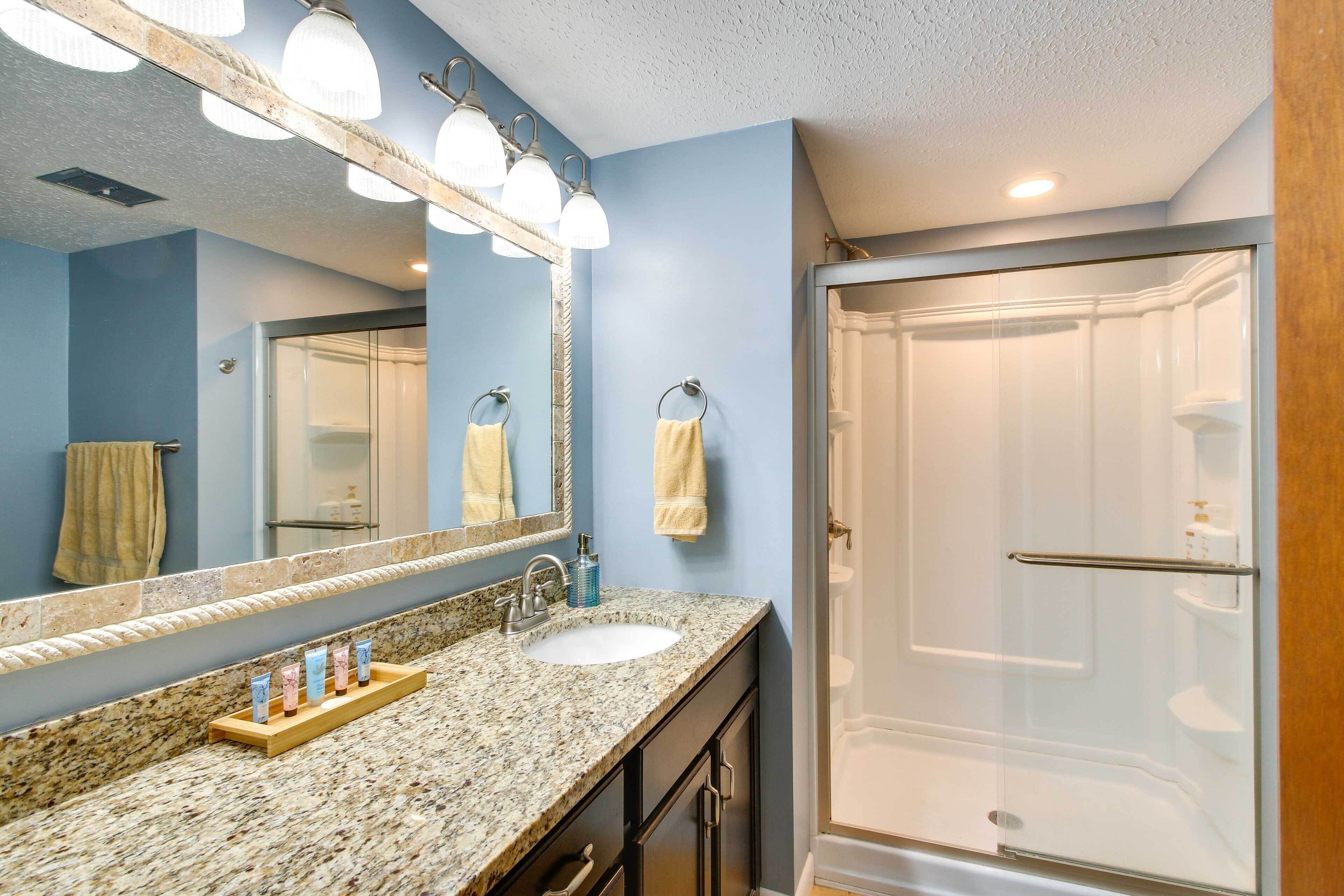 A bathroom with a granite countertop, a sink, a mirror with lights, and a glass-enclosed shower.