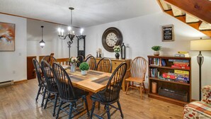 A dining area with a wooden table and chairs, a chandelier, a clock, and a bookshelf with books and games. - 1 Mi to Downtown Conway: Spacious Family Condo! (North Conway)