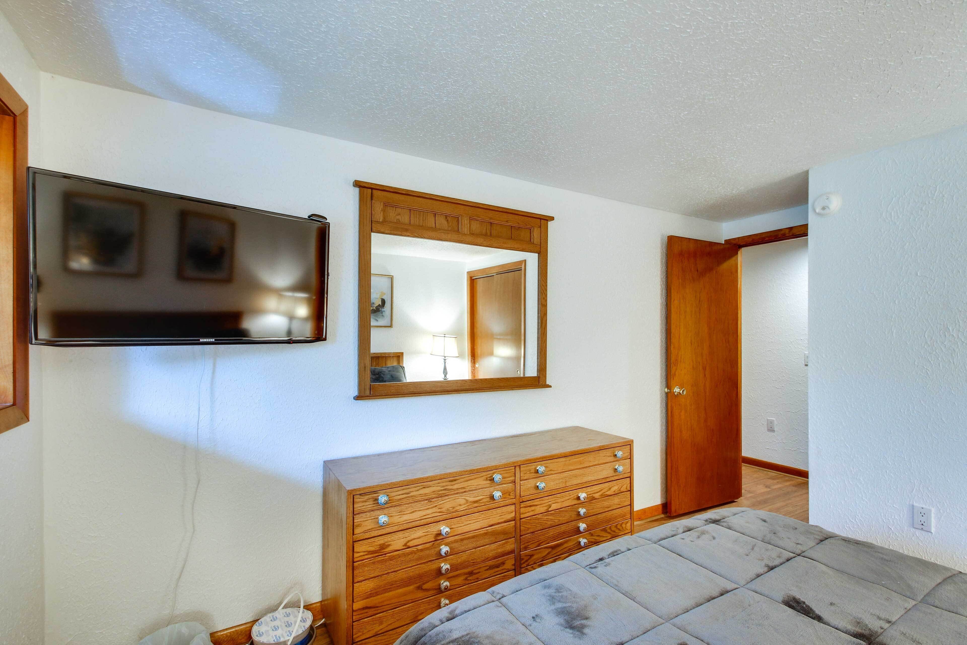 Une chambre à coucher avec une commode en bois, un téléviseur à écran plat fixé au mur et un miroir au-dessus de la commode.