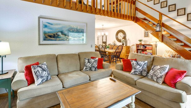 A spacious living room with a wooden staircase, a dining area, and a large painting on the wall. - 1 Mi to Downtown Conway: Spacious Family Condo! (North Conway)