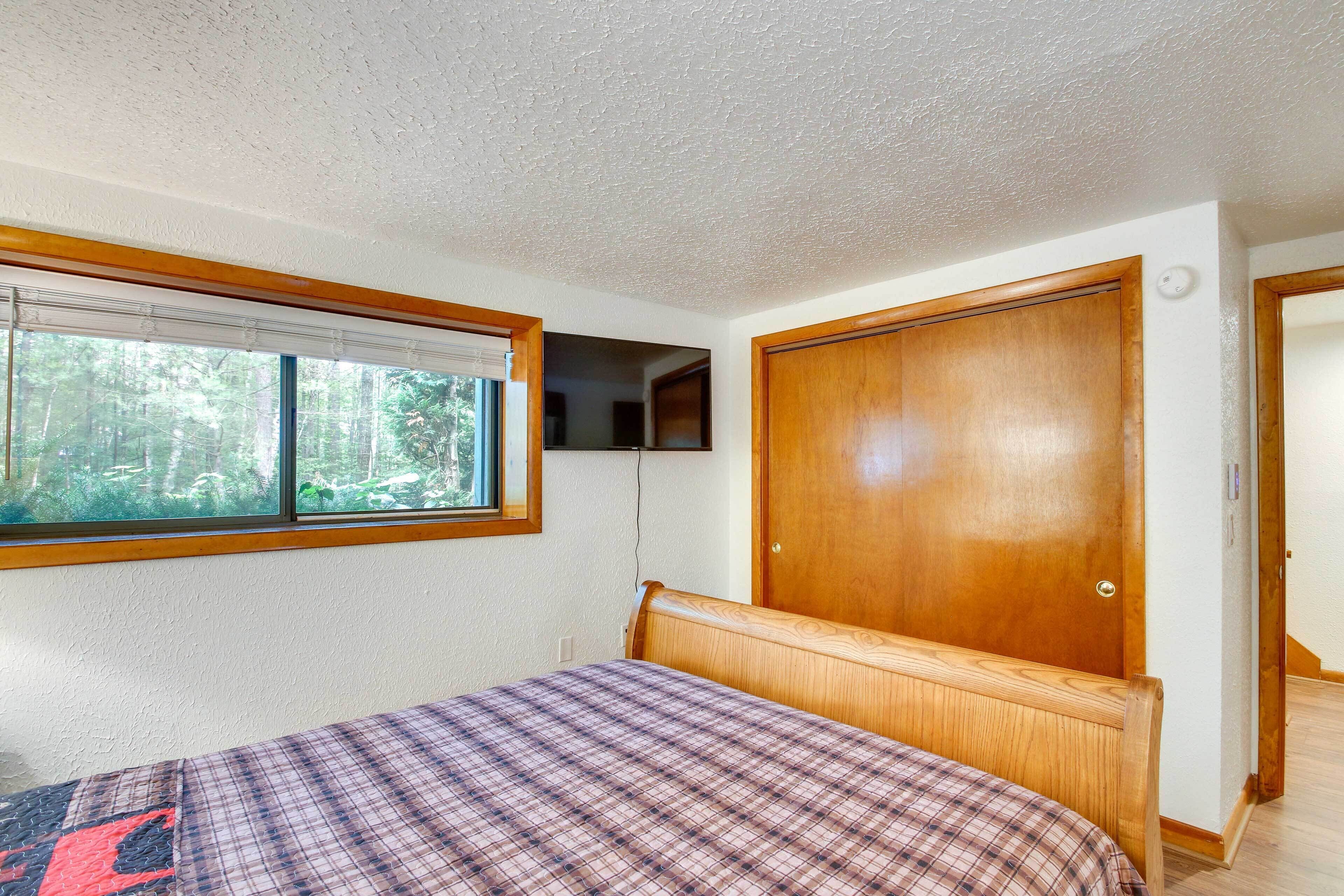 A bedroom with a bed, a window with a view of trees, a wooden door, and a white ceiling.