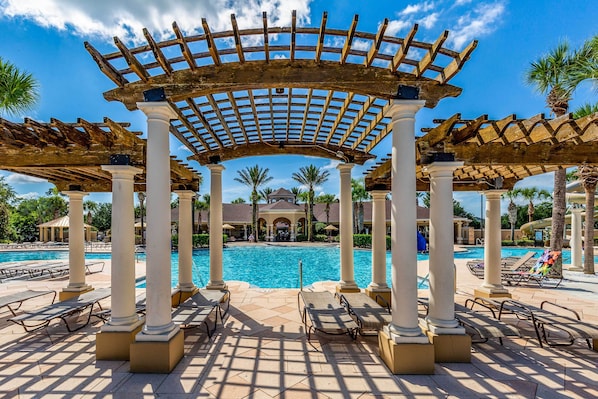 Un espace piscine agrémenté d’une pergola, de chaises longues et offrant une vue sur un bâtiment en arrière-plan.