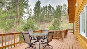A wooden deck with a table and chairs, overlooking a forested hillside.